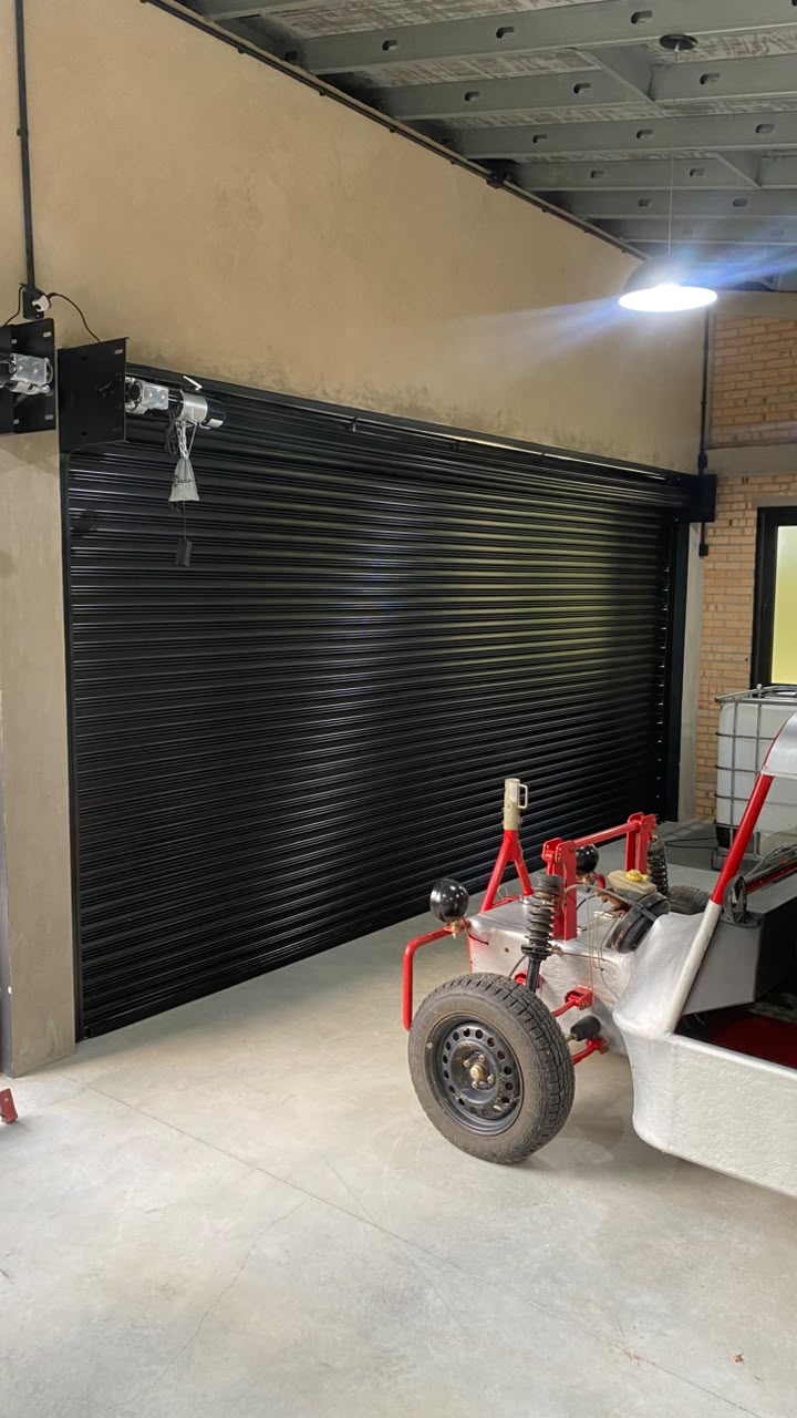 Porta de enrolar automatizada preta instalada por dentro do vão, vista da parte interna com o motor no topo