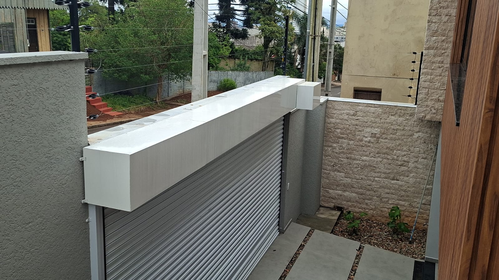 Porta de enrolar automatizada em área externa com fechamento de rolo e motor em branco